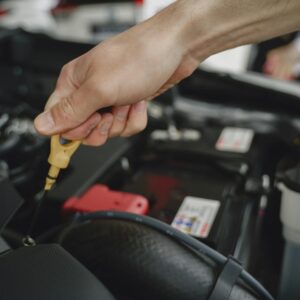 Hand holding oil dipstick over car engine