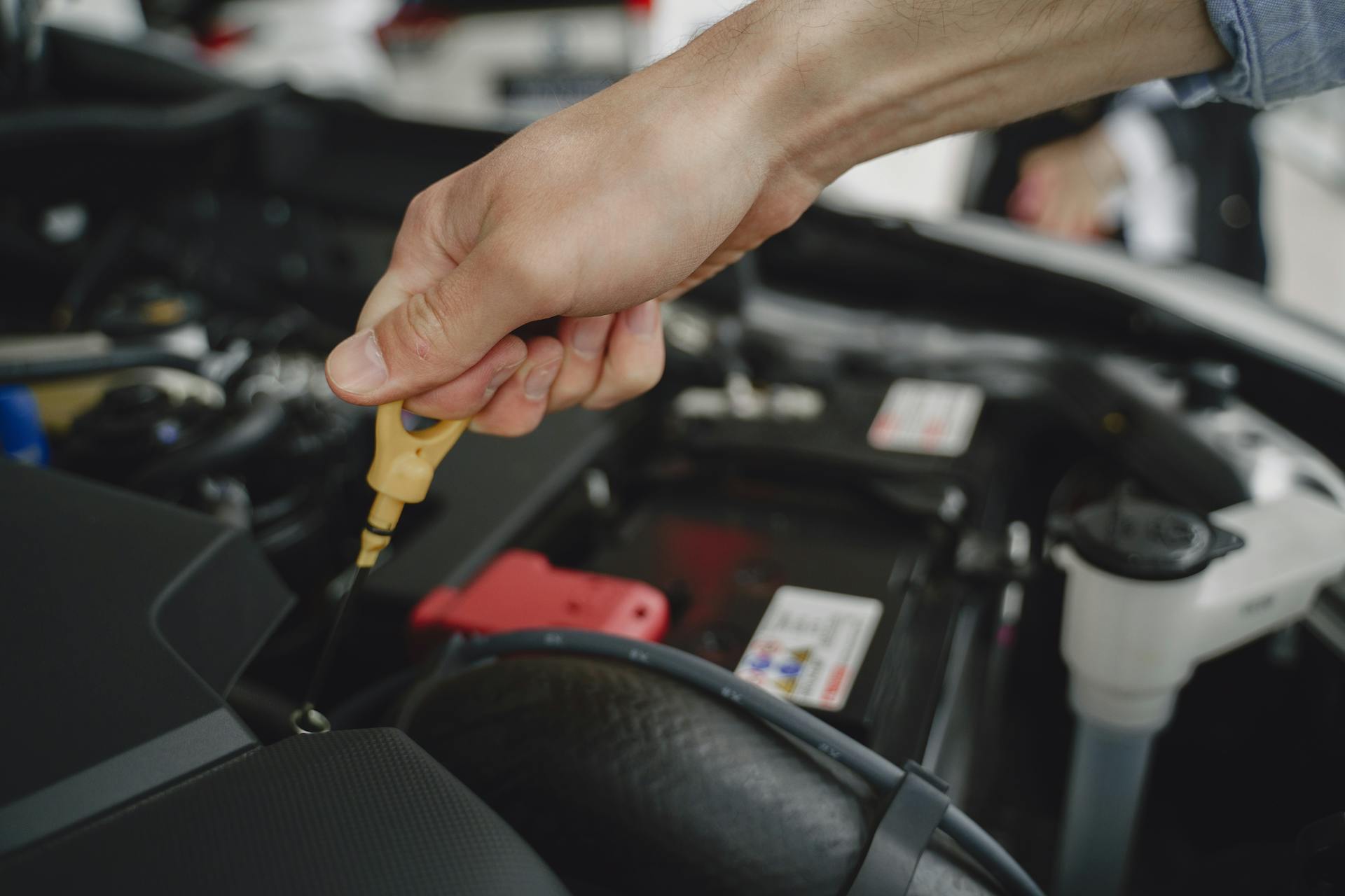 Hand holding oil dipstick over car engine